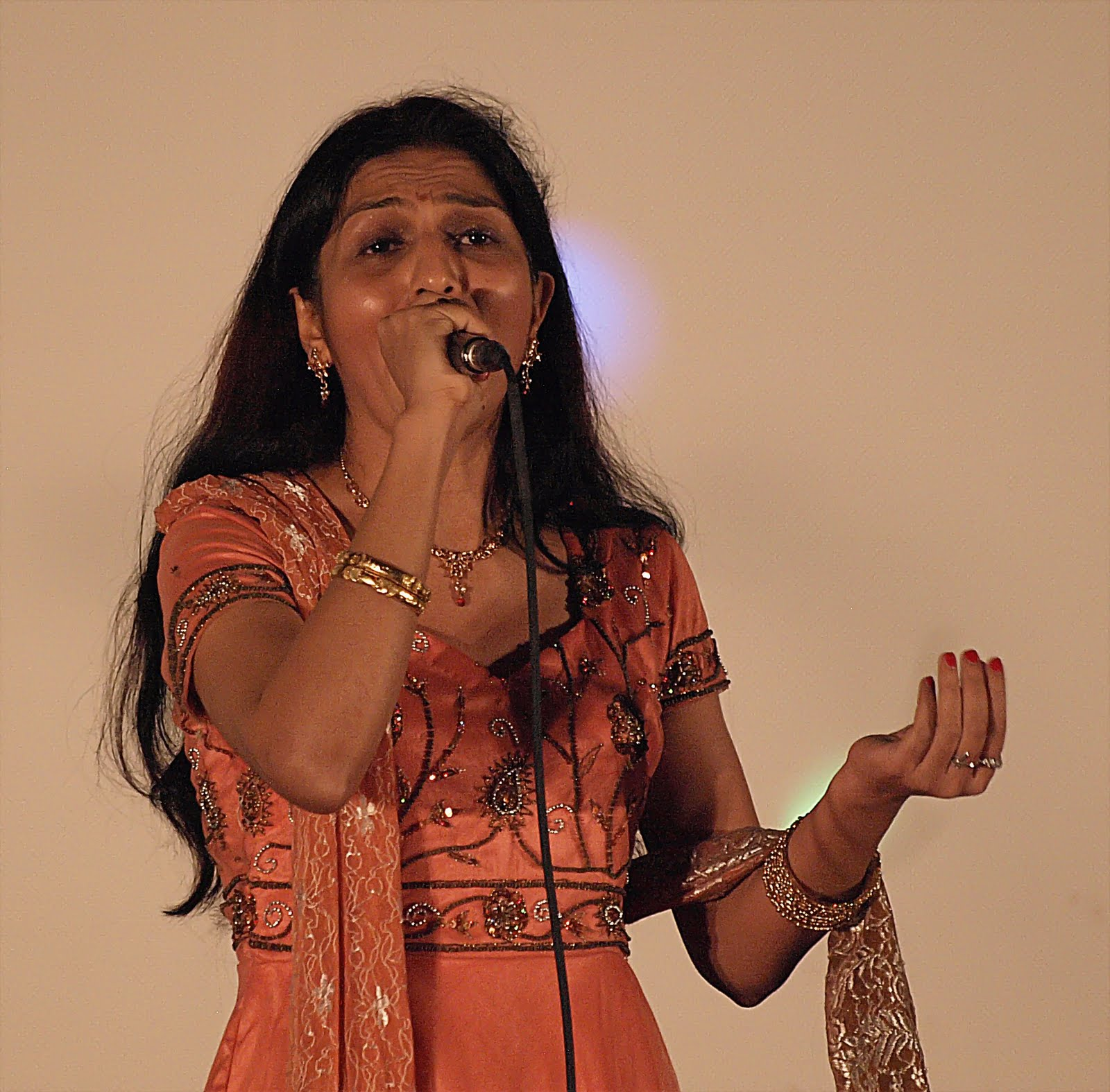A woman in an orange outfit, singing expressively