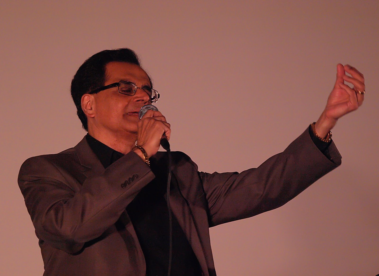 A performer in a brown jacket, singing with an animated gesture