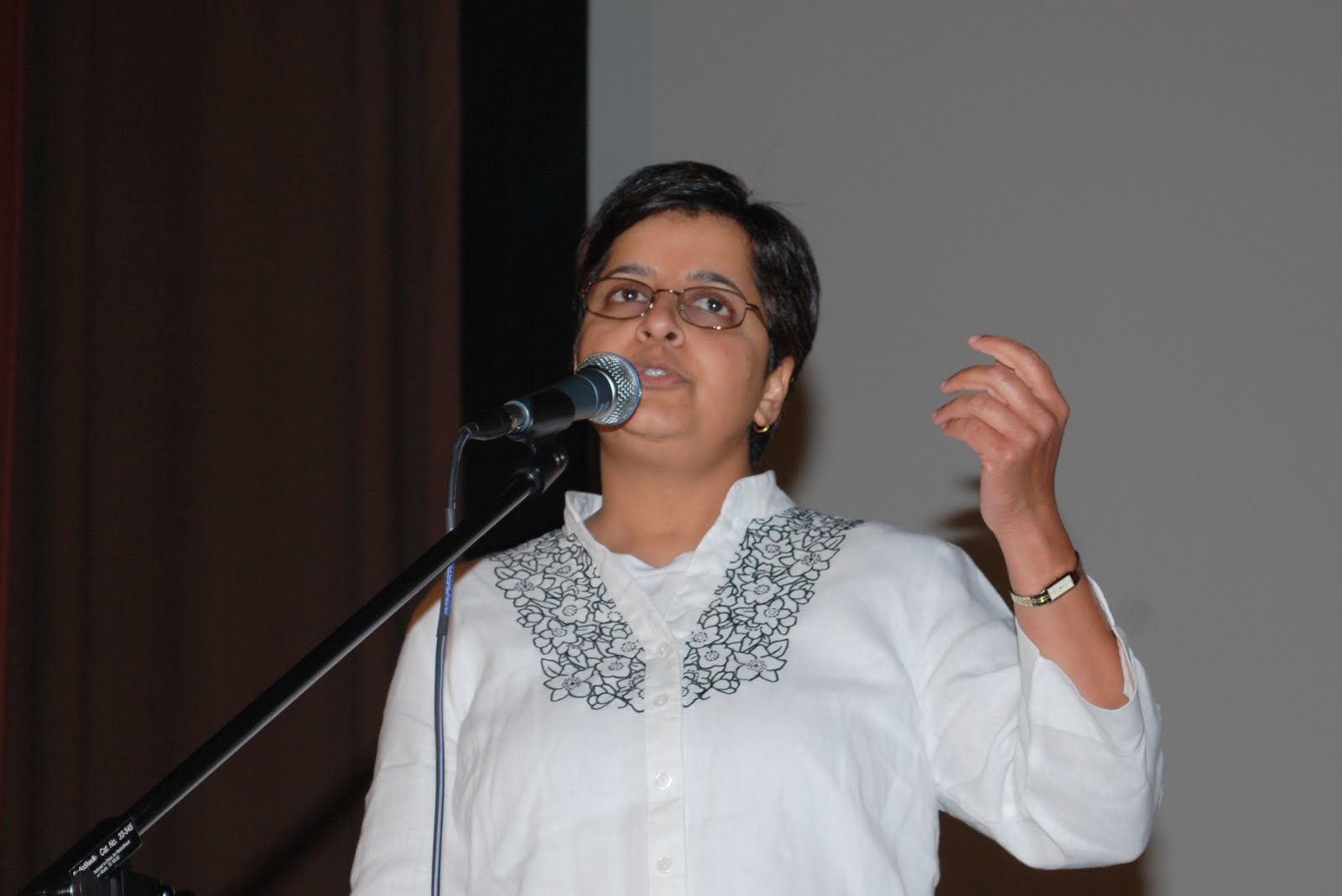 A performer in a white kurta, singing with an animated gesture