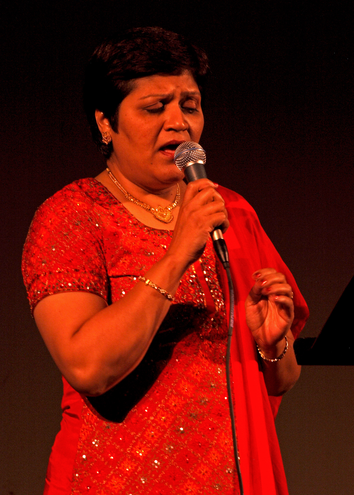 A woman in a red sari singing into a microphone