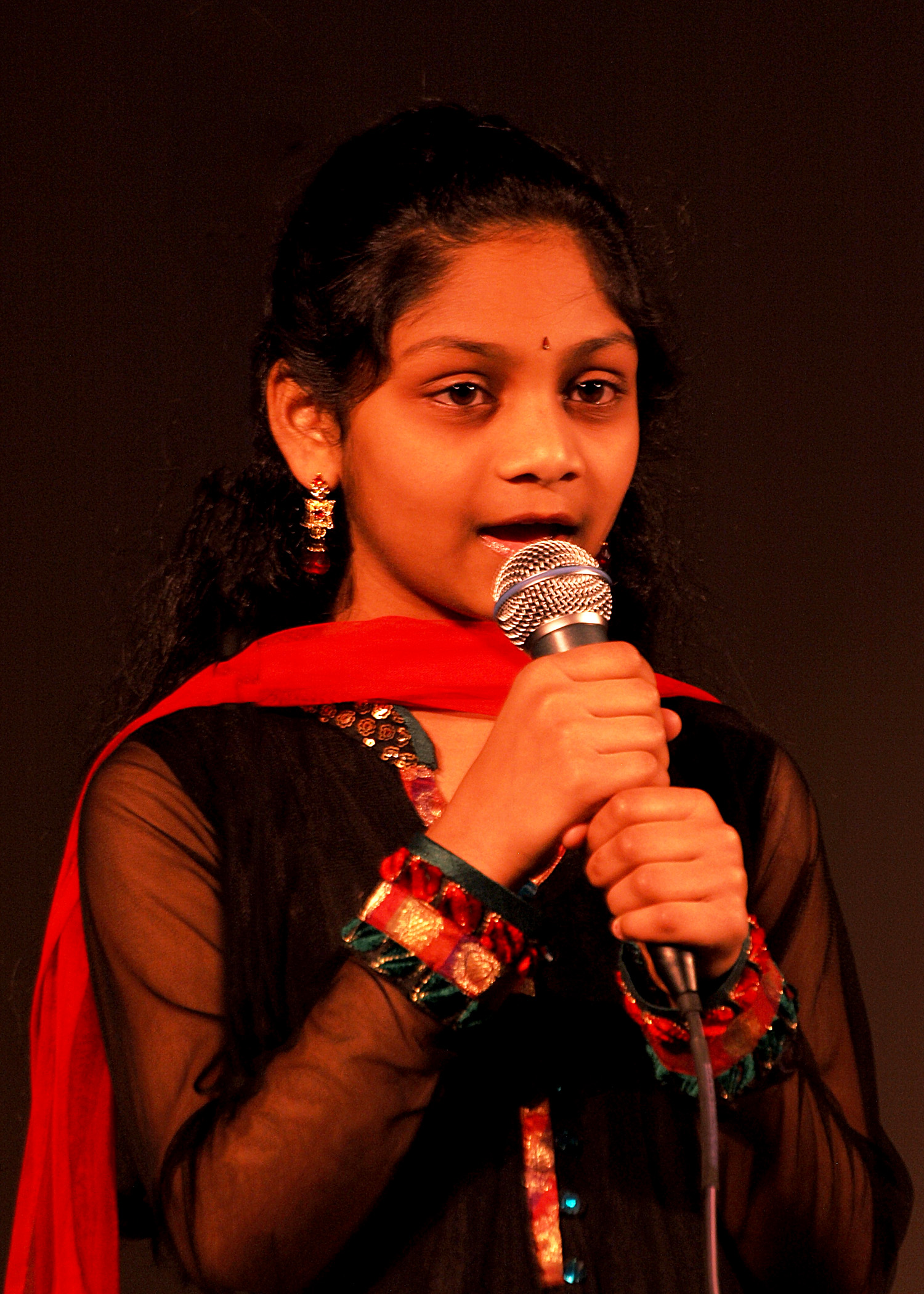A young girl singing, wrapped in a red shawl