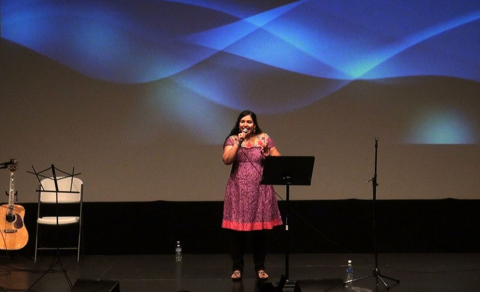 A woman singing in front of a blue backdrop
