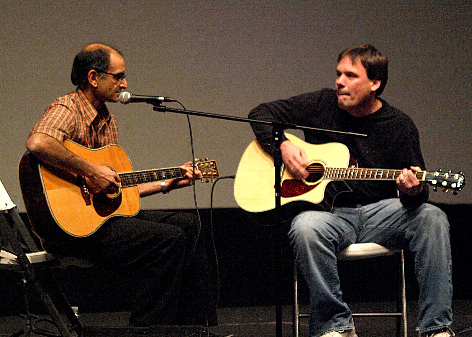 Two men playing acoustic guitars together on stage