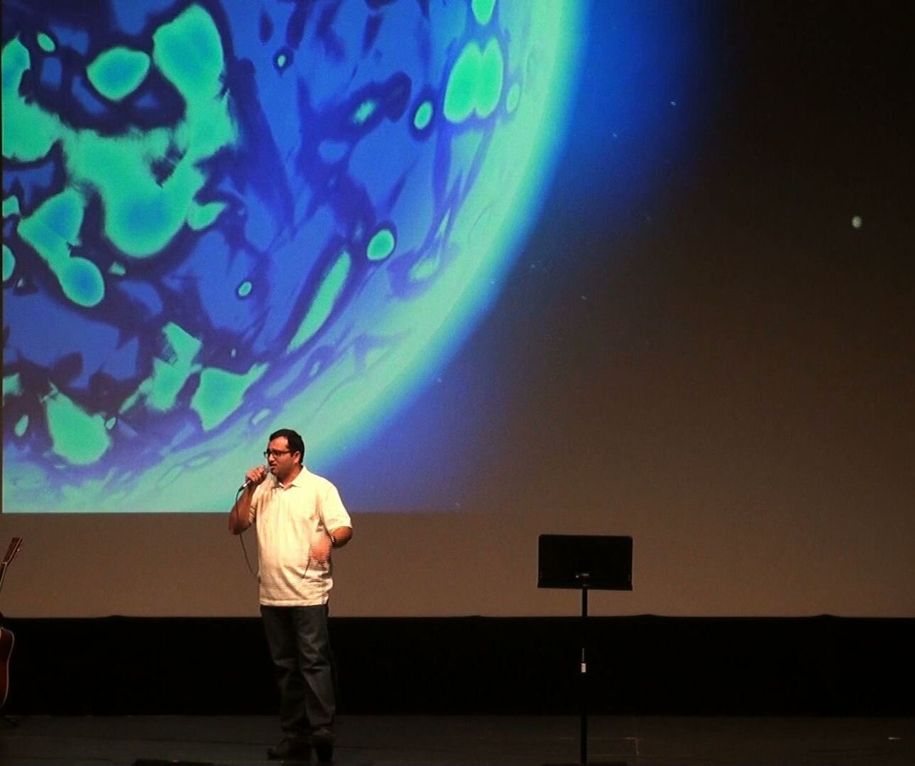A man singing in front of a blue-green backdrop
