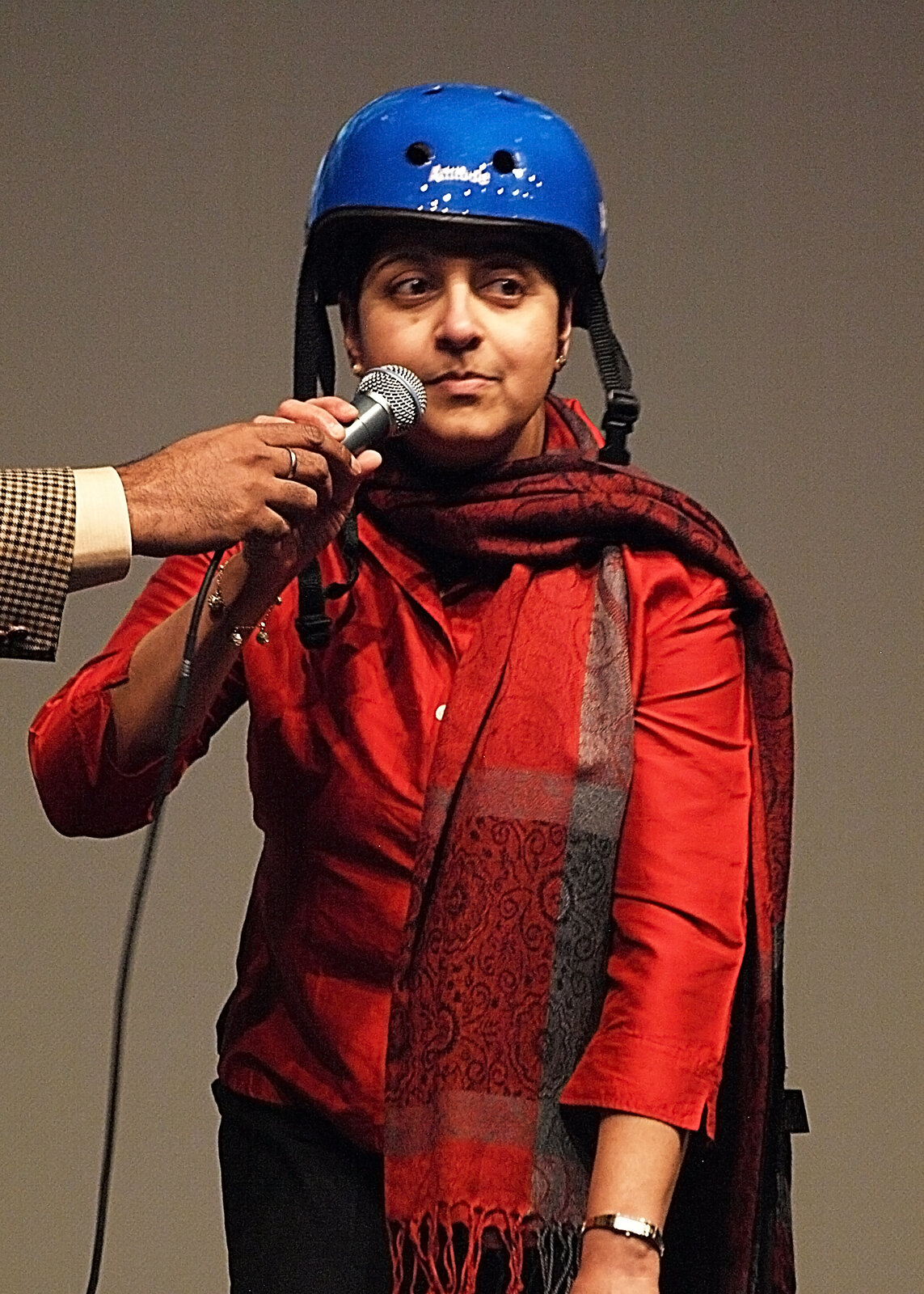 A woman in a red top and blue helmet singing