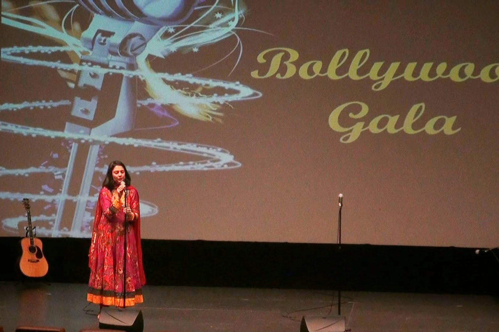 A woman in red singing in front of the Bollywood Gala backdrop