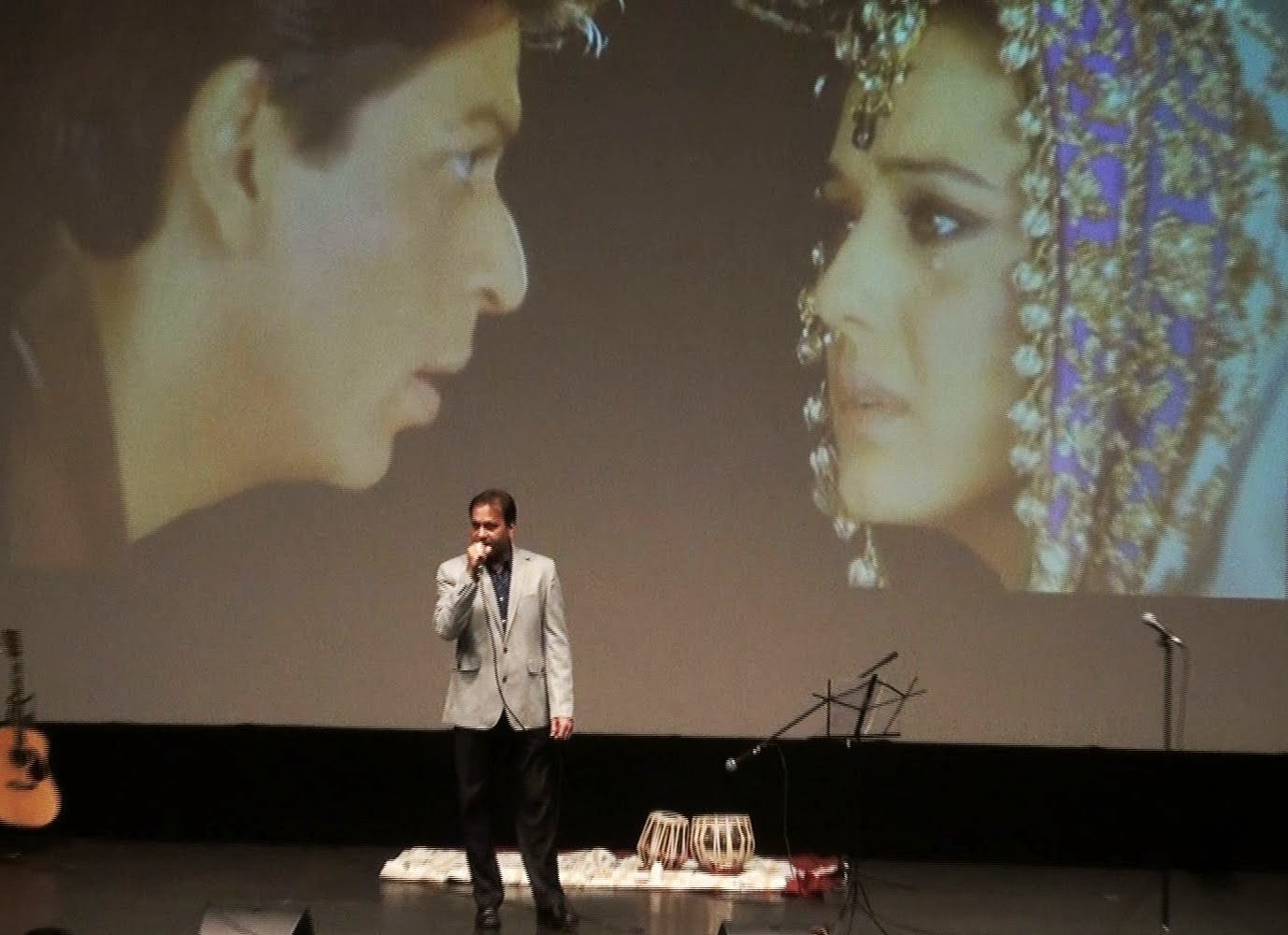 A man singing in front of a projected film clip