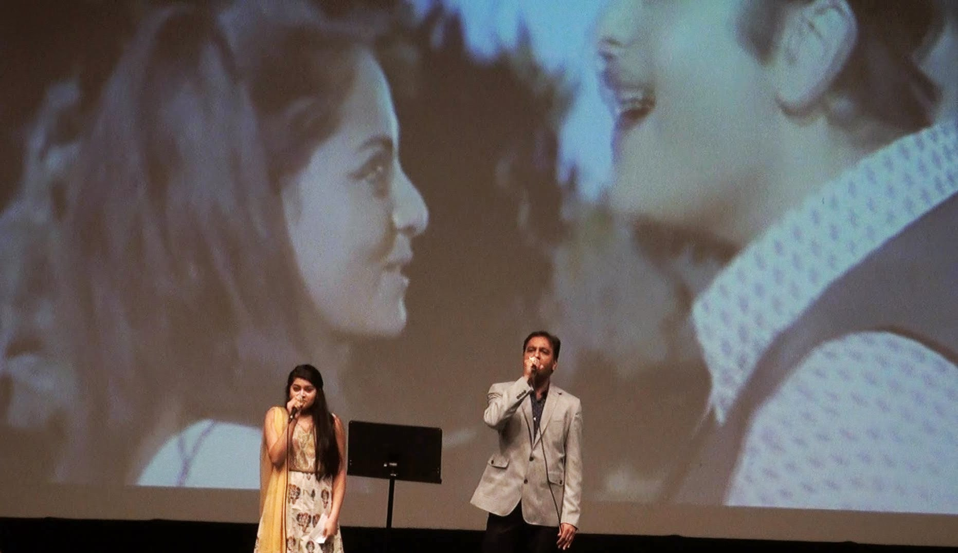 Two performers singing a duet in front of a projected film clip
