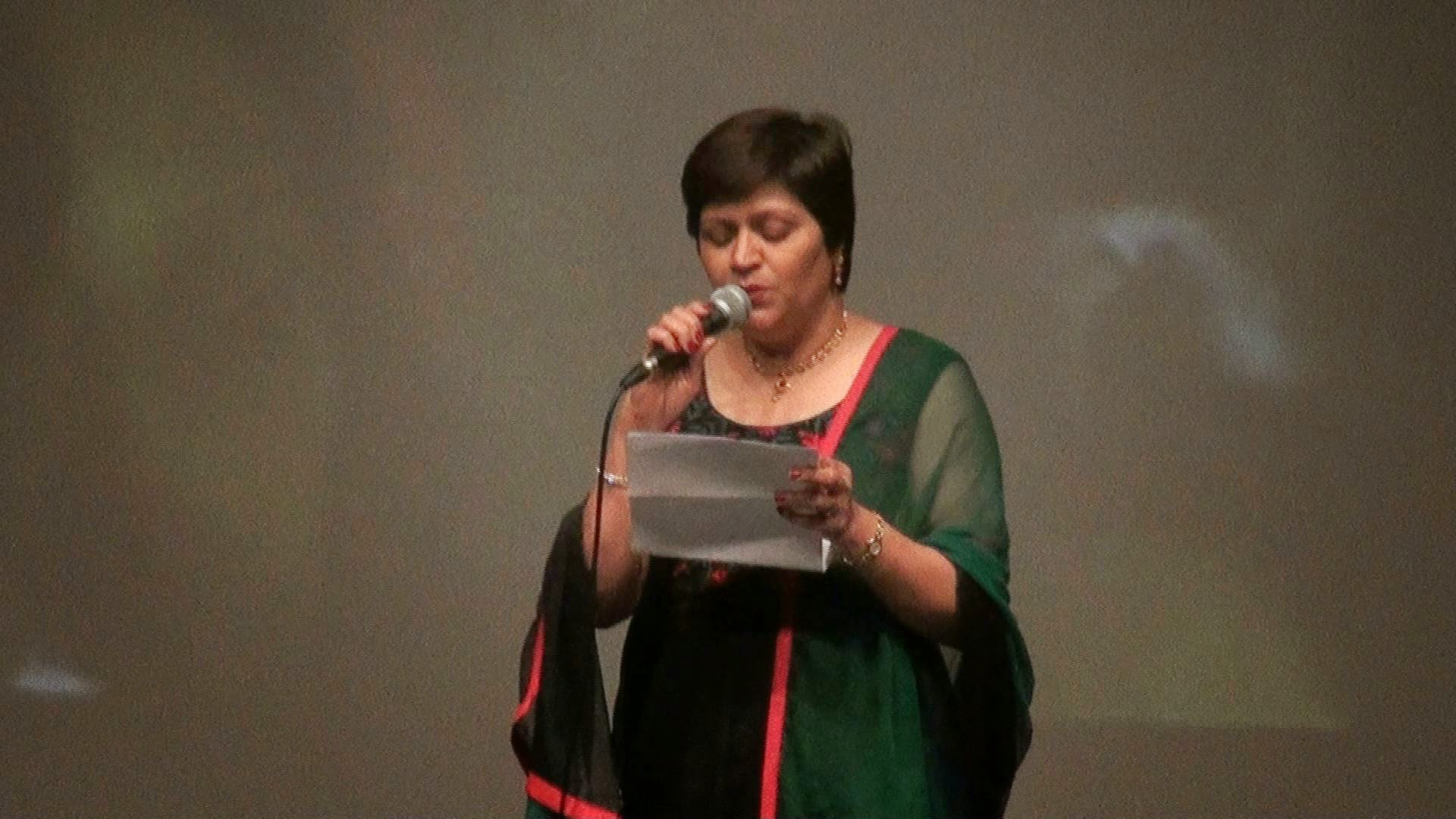 A woman reading from a program on stage