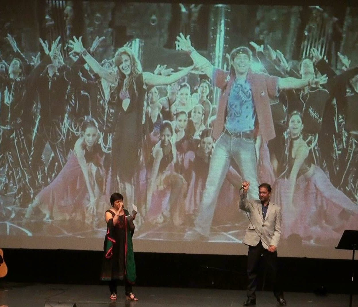 Two performers singing a duet in front of a projected film clip