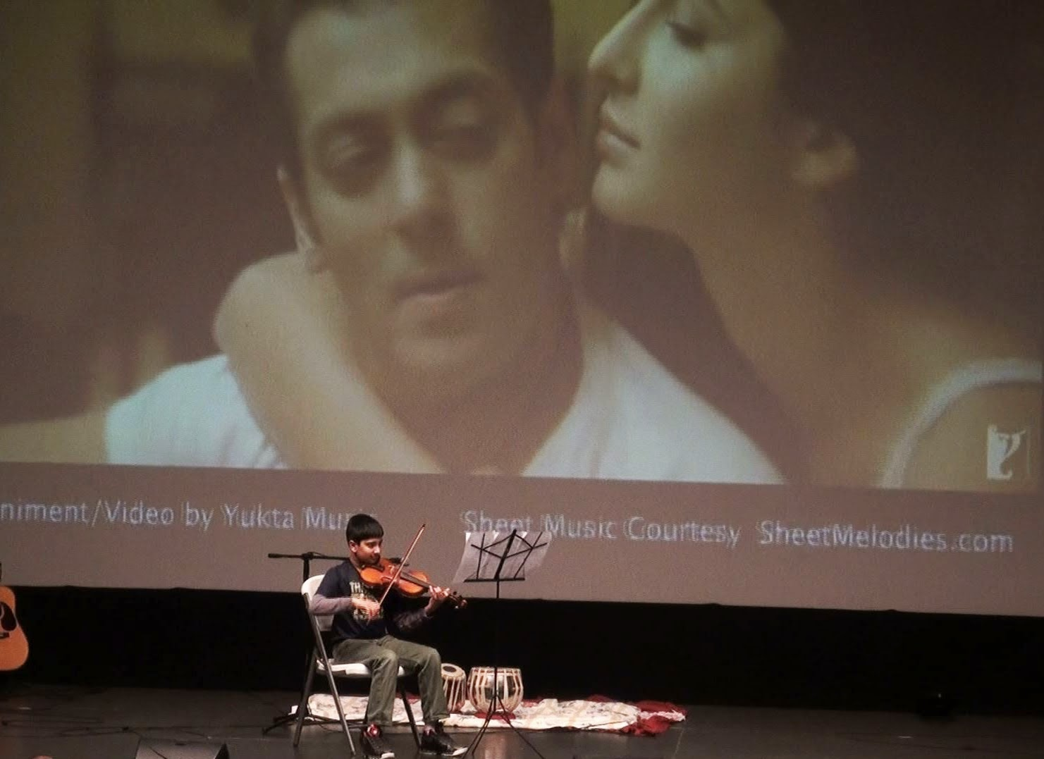 A man playing violin in front of a projected film clip