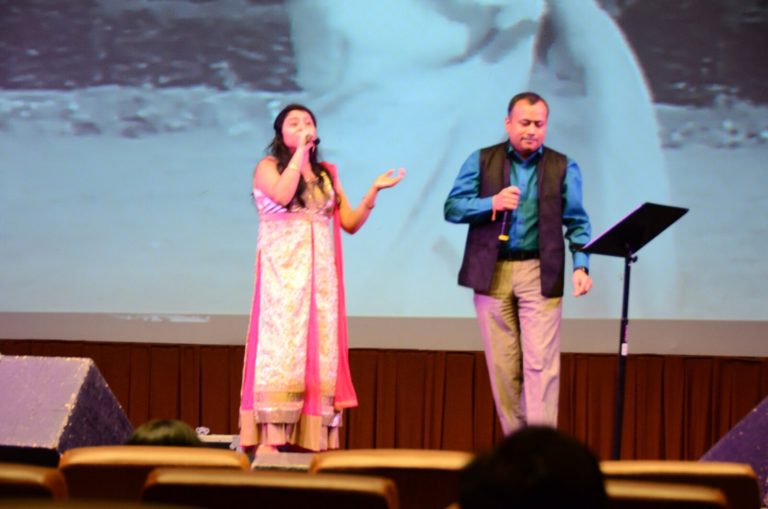 A woman in a pink and gold outfit singing with a man beside her