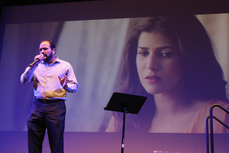 A man singing with a film scene projected behind him