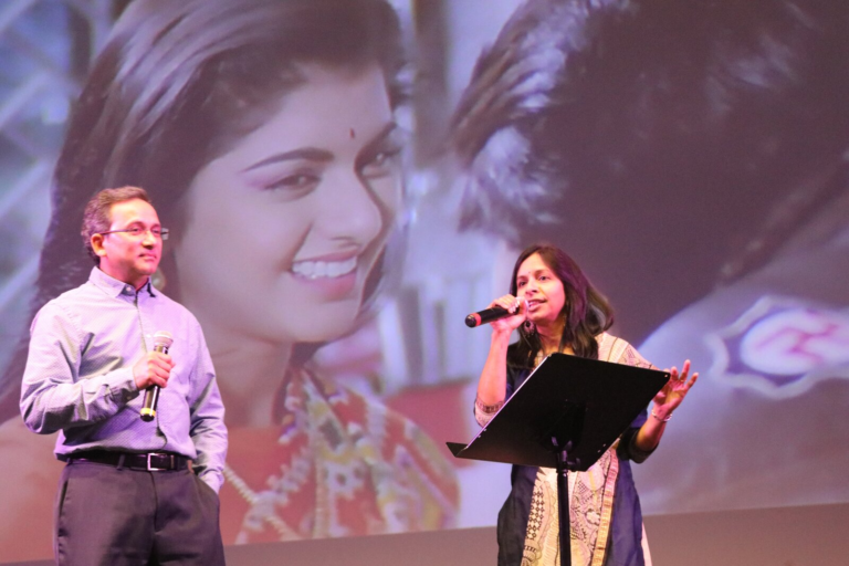 A man singing with a projected image of a couple behind him