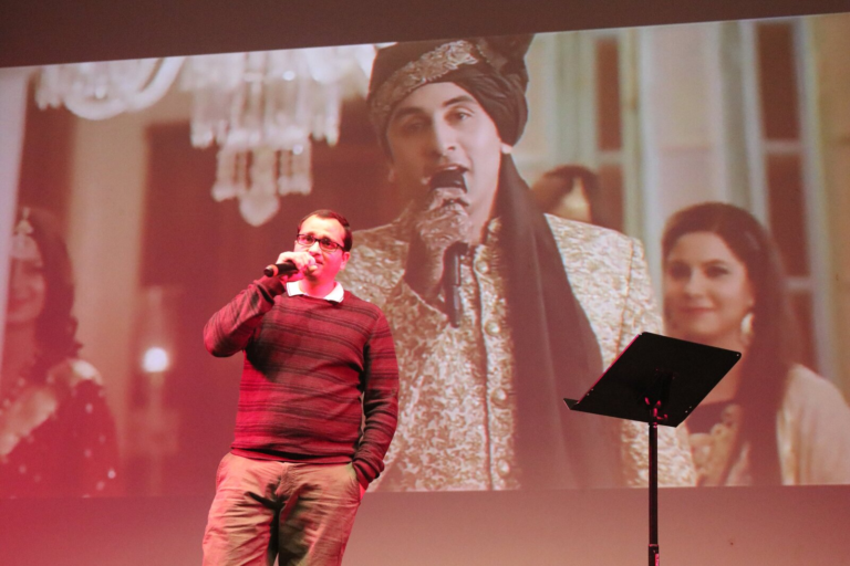 A man singing with a projected image of a couple in traditional dress behind him