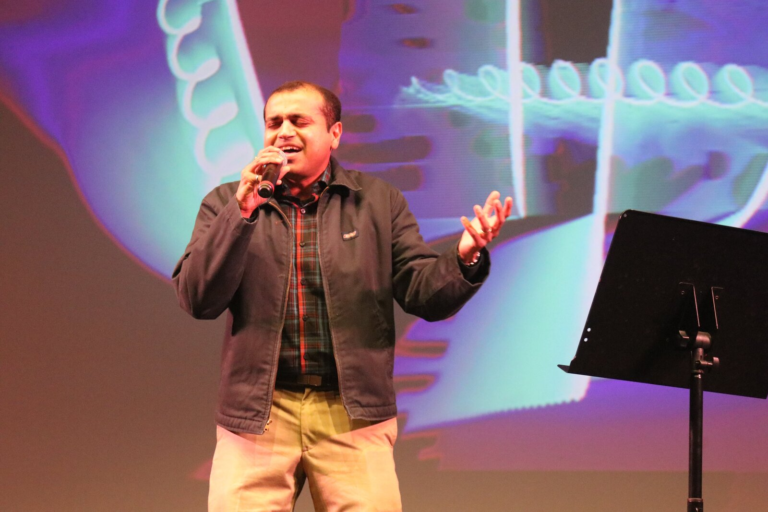 A man singing in front of a blue swirl backdrop