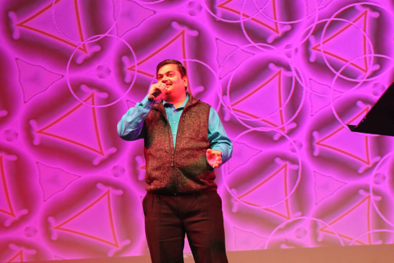 A man singing in front of a purple and pink patterned backdrop