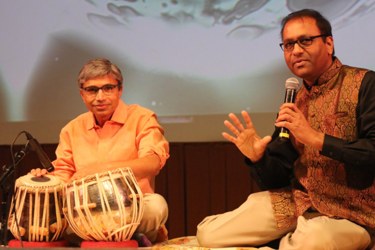 A man playing tabla while another man sings beside him