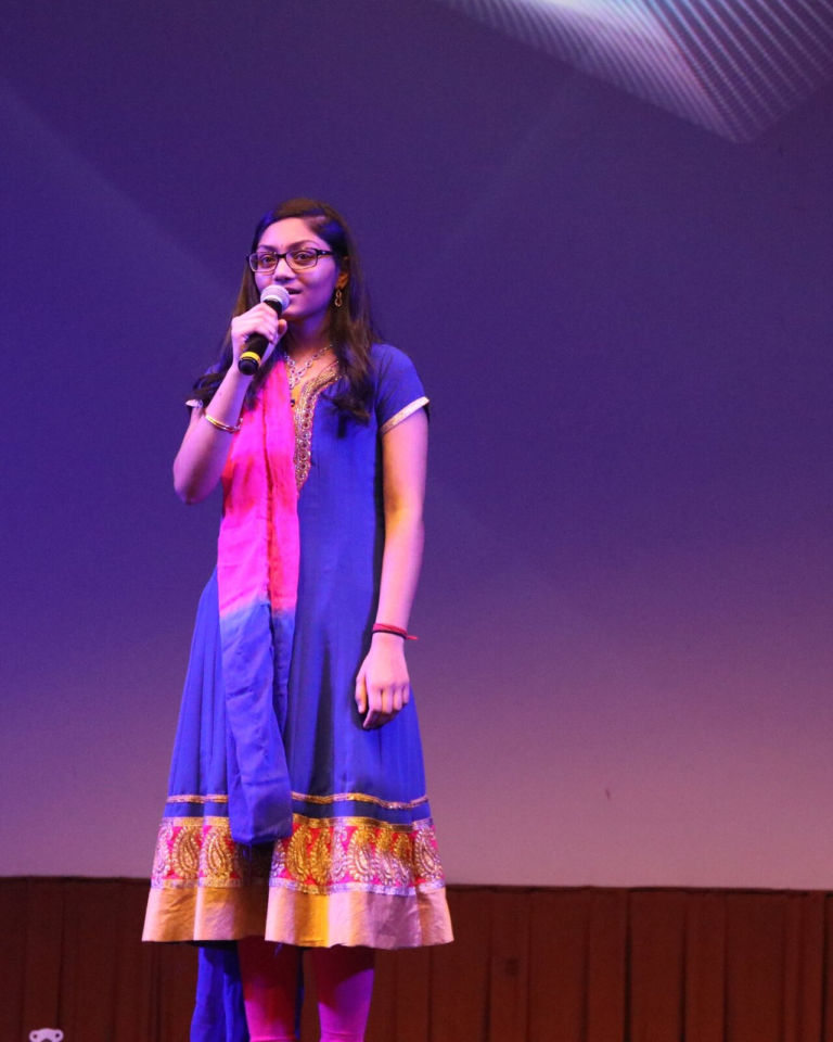 A young woman in a blue and pink outfit singing