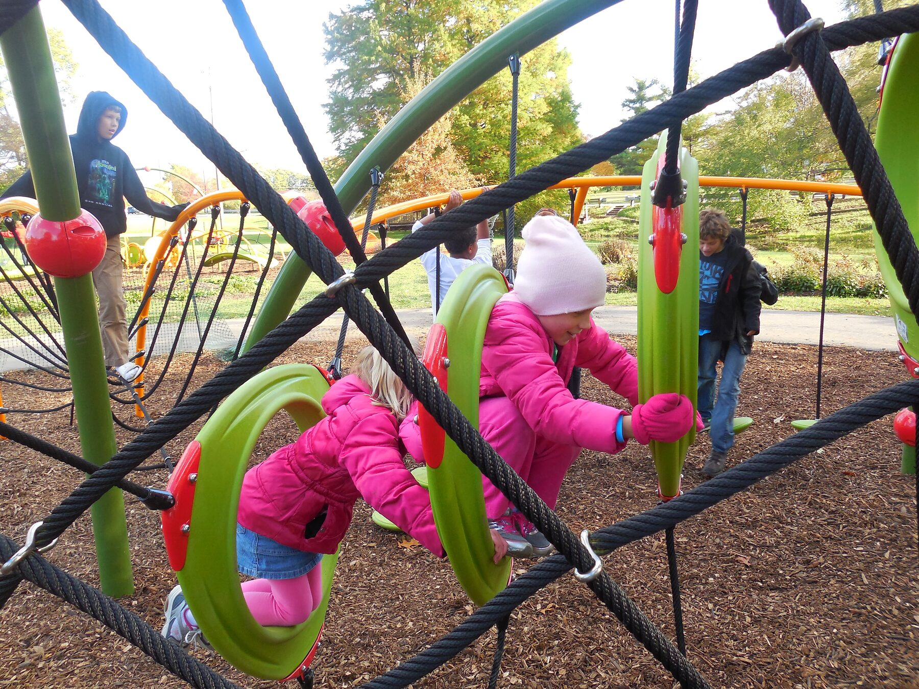 Two children in pink winter coats climbing the rope net at Butterfly Meadow
