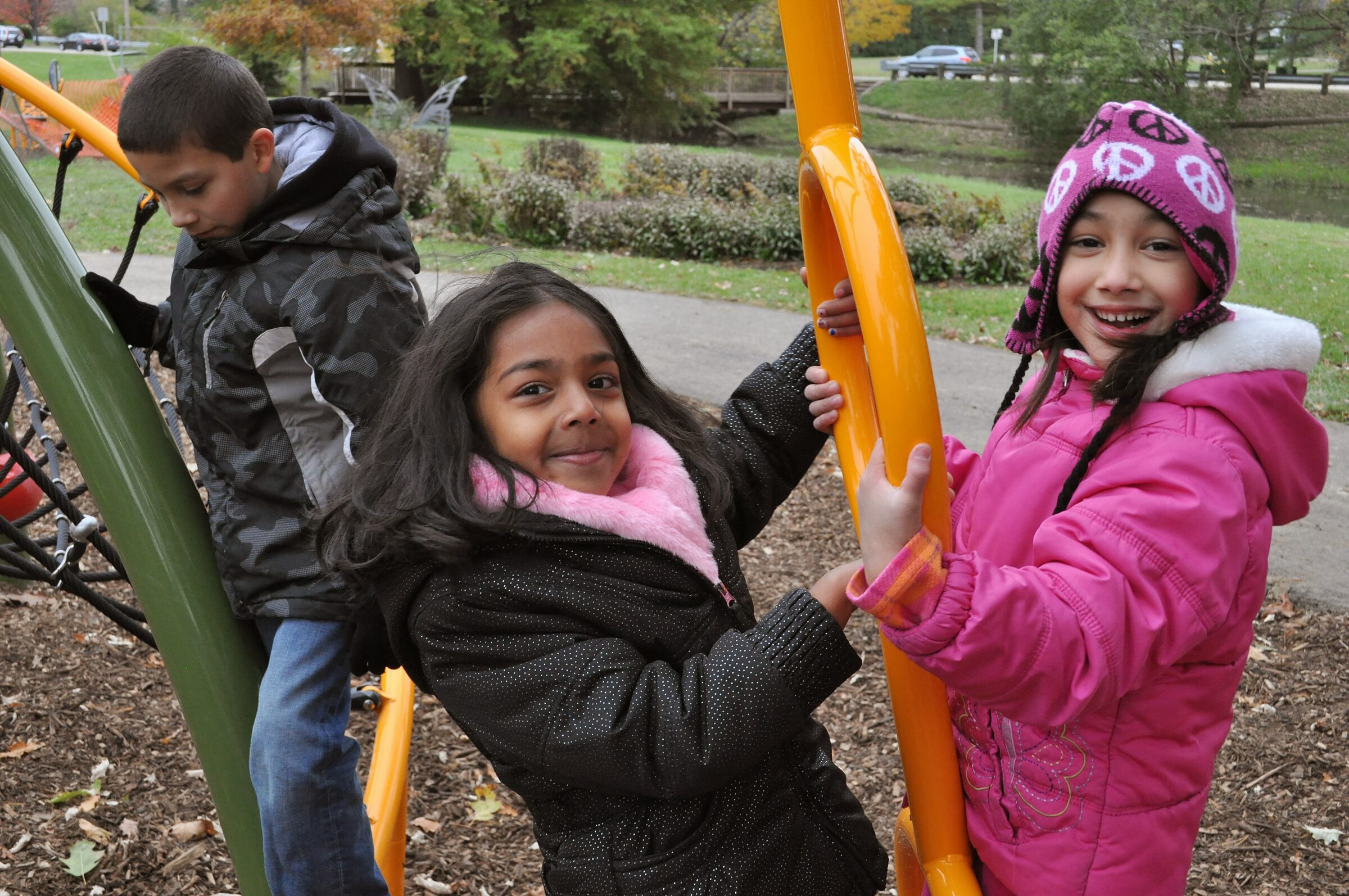 Three children laughing as they climb the yellow and green play structure at Butterfly Meadow
