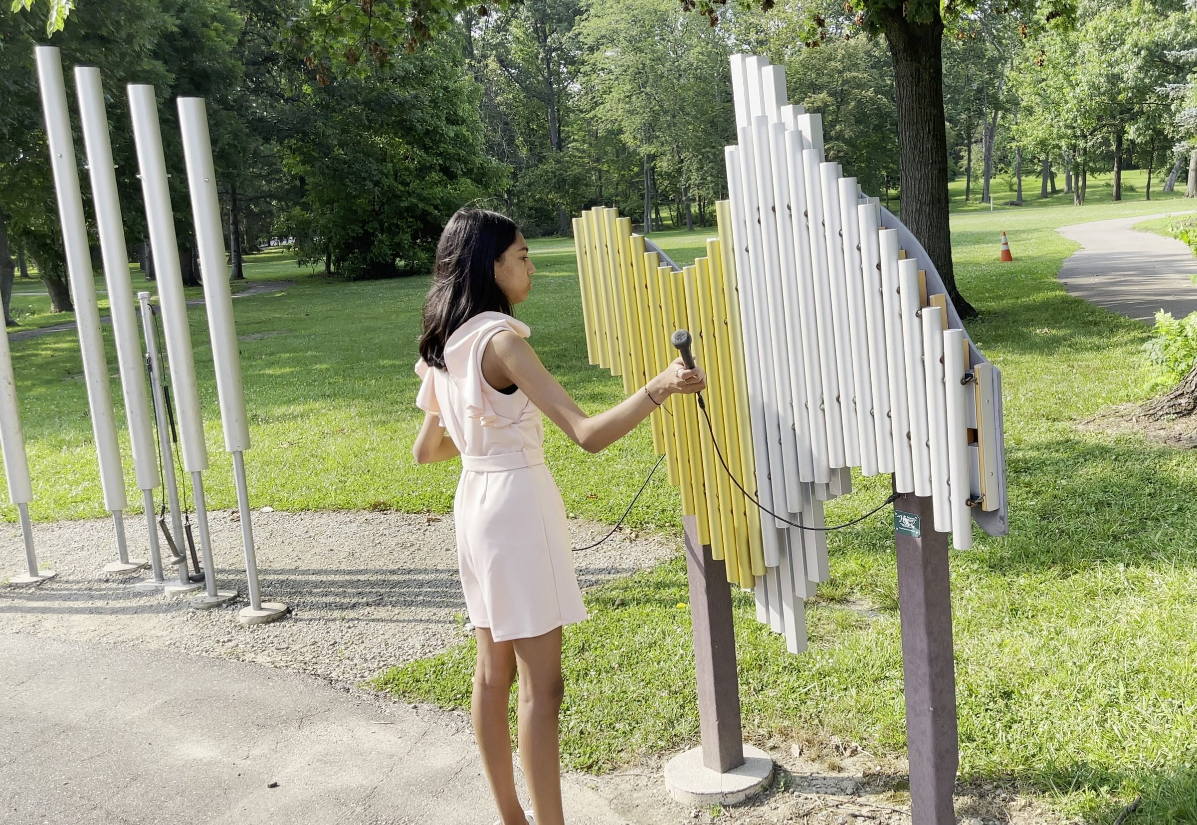 A girl playing The Swirl, the yellow and silver sculptural chime instrument at Nature Sounds, with the nine-foot chimes standing behind her
