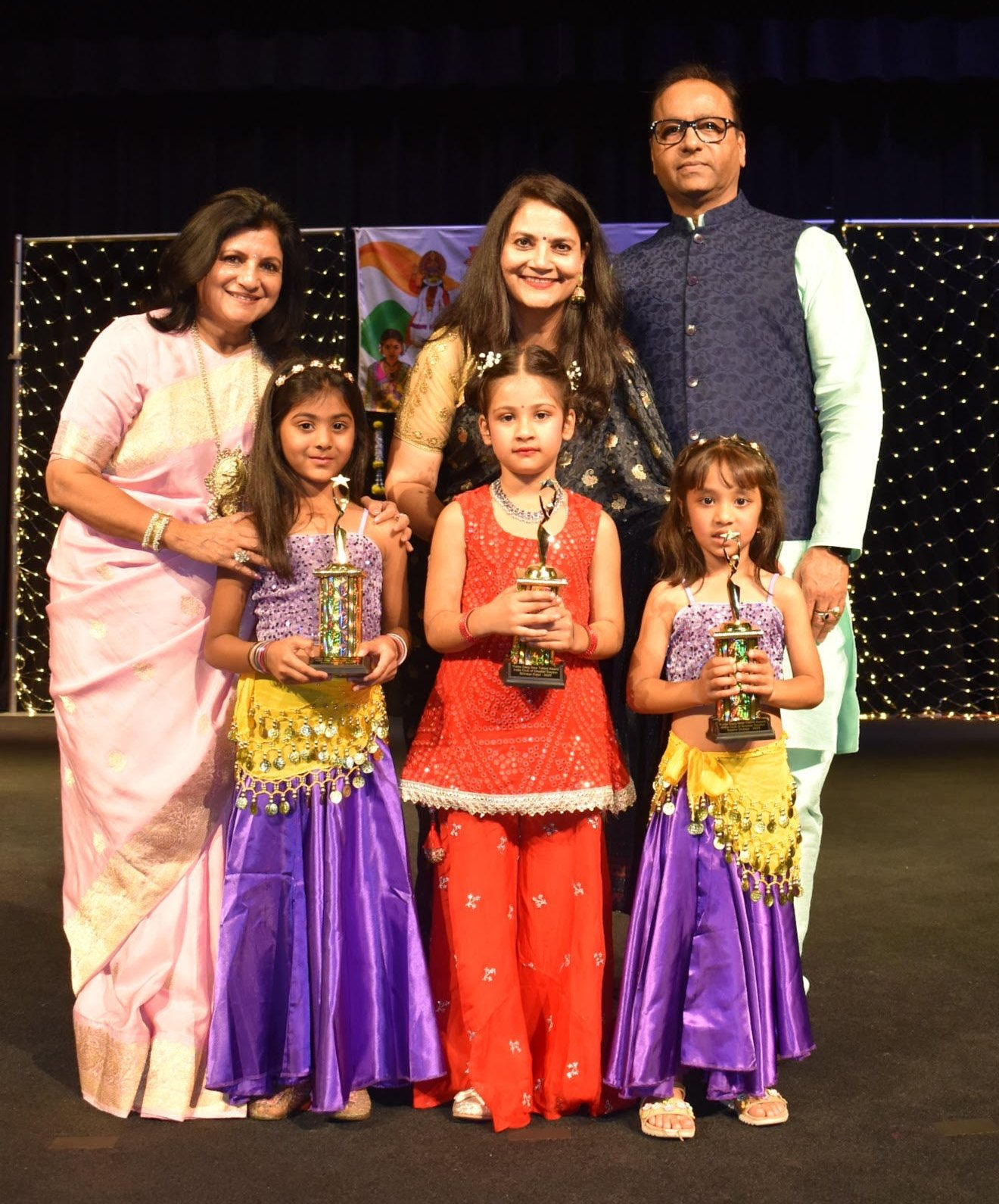 Three young awardees holding their trophies on stage at the 19th Yukta Garg New Talent Awards, with the presenters standing behind them