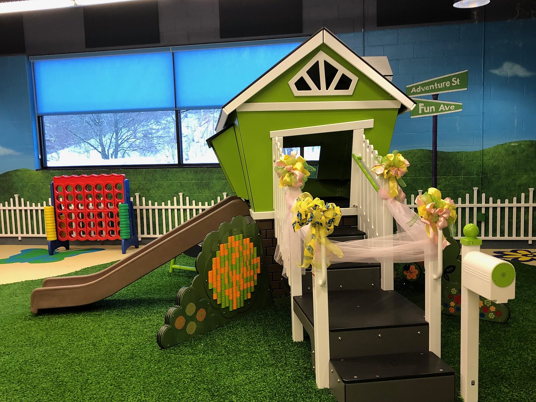 The green play cottage at Yukta’s Garden, decorated with ribbons and bows for its opening, with a slide, giant Connect Four and artificial turf around it