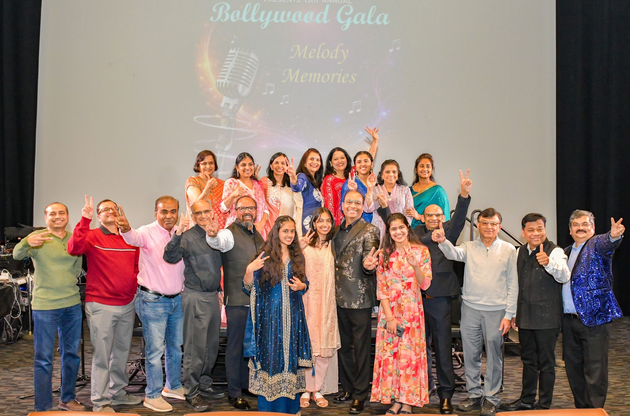 Singers from the 13th annual Bollywood Gala on stage together — children and adults, in front of a screen reading Bollywood Gala: Melody Memories