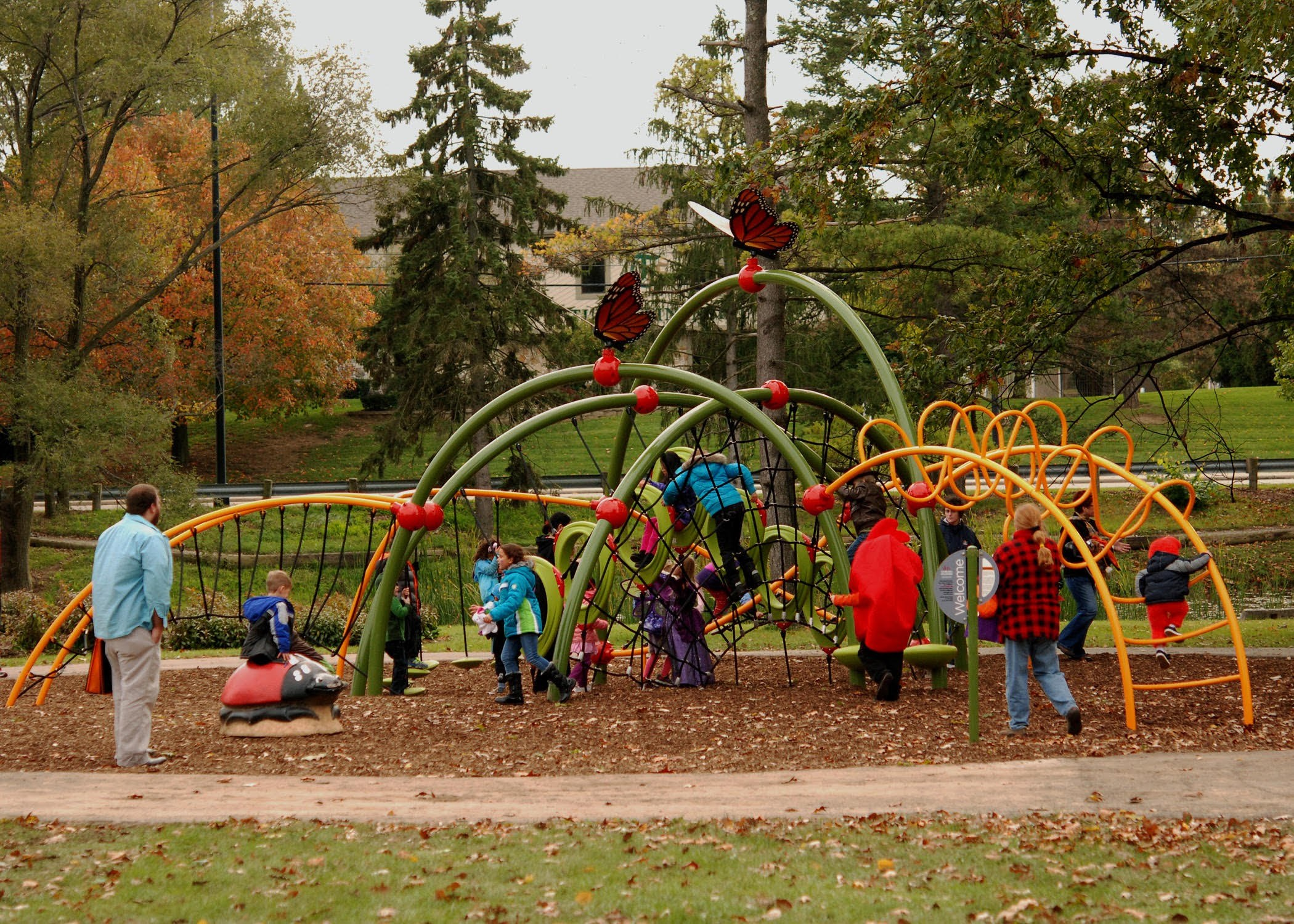 Children climbing the arched Butterfly Meadow play structure on a fall day, with monarch butterfly sculptures overhead